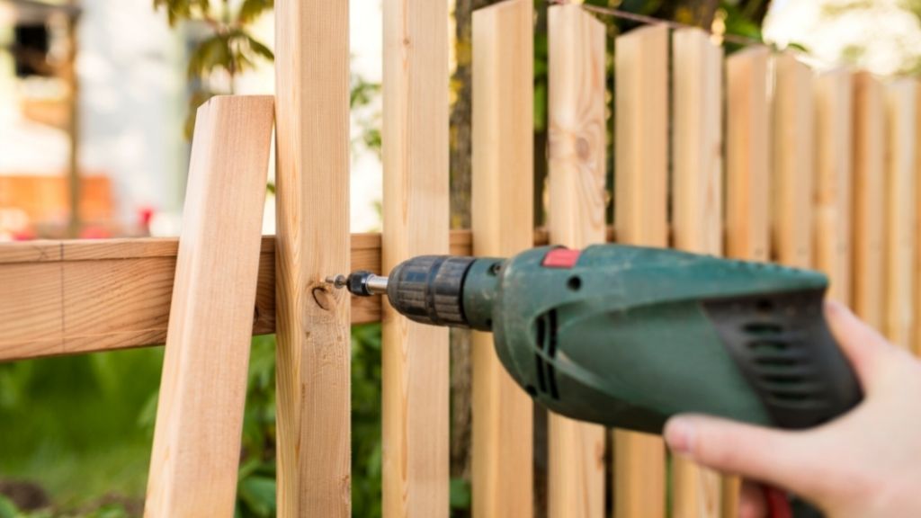 Hand håller i skruvdragare som fäster nytt staket runt trädgården.